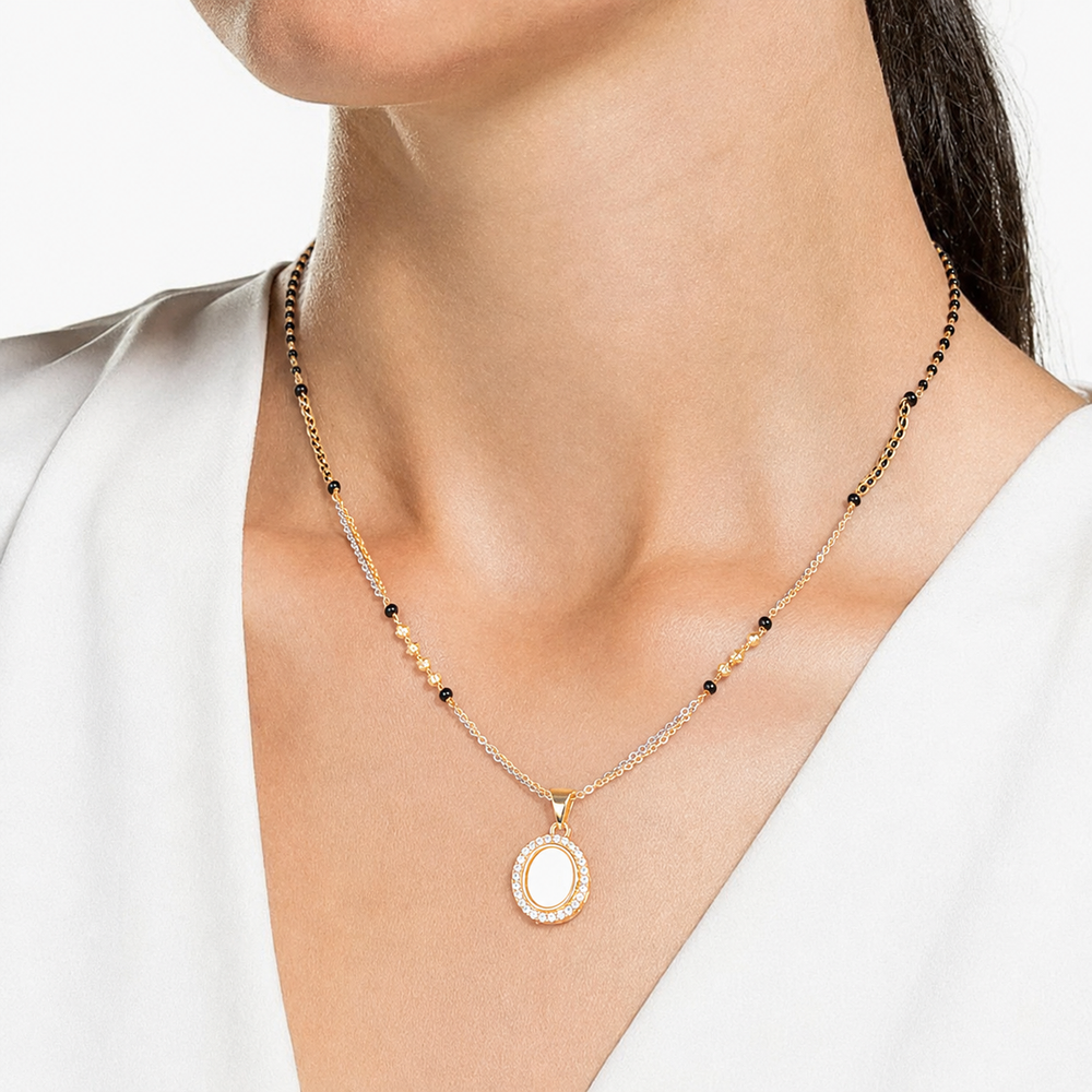 A close-up of a model wearing a delicate gold necklace with a white oval pendant and small black bead accents on a white top.