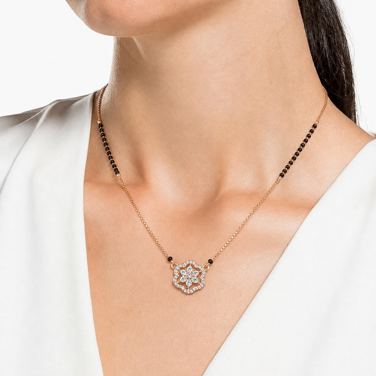 A close-up of a model wearing a delicate rose gold necklace with a floral starburst pendant. The necklace features a gold-toned chain with small black beads spaced along the sides, and a central pendant set with clear stones in a rose gold setting.